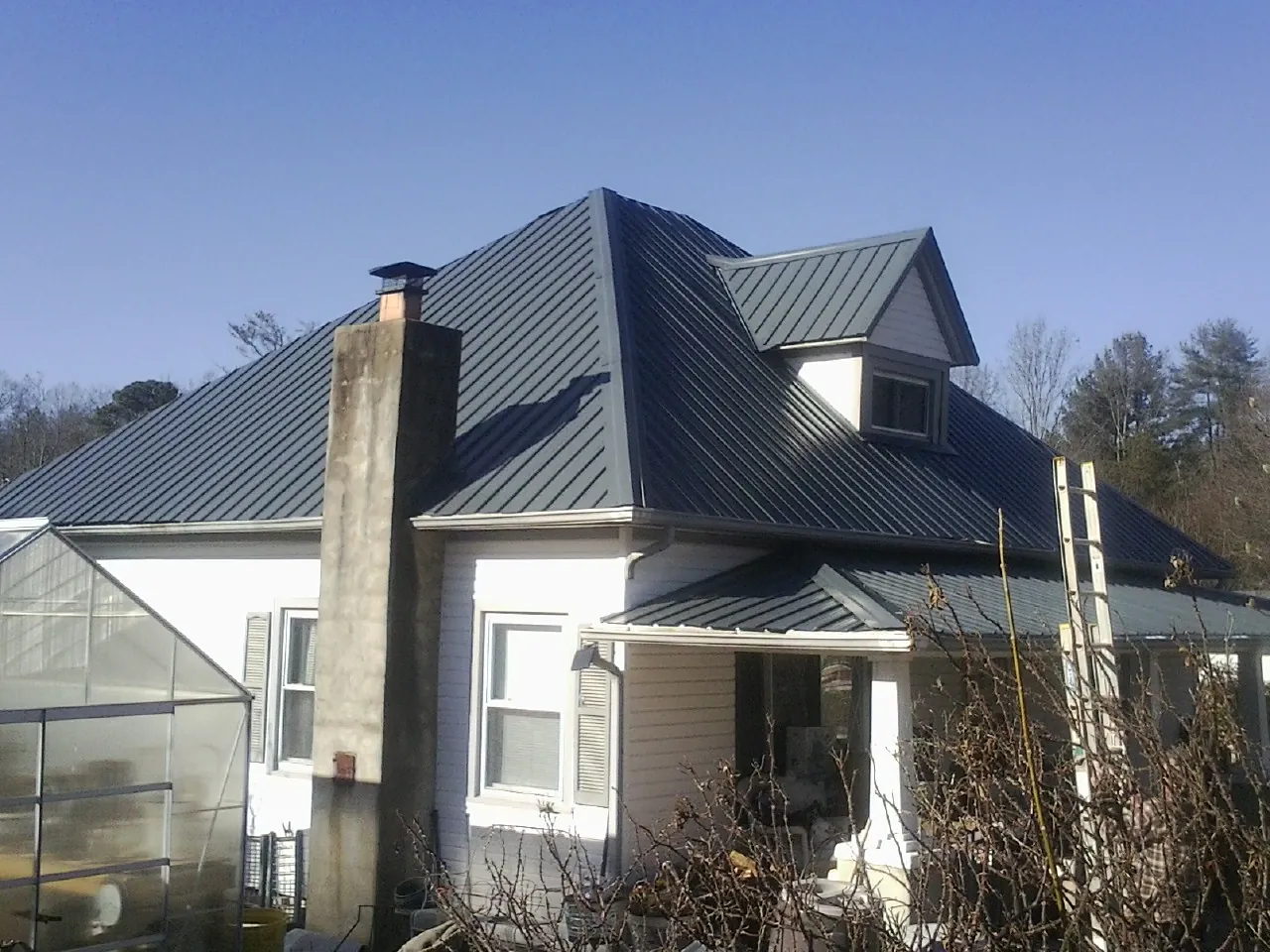 Dark blue standing seam metal roof on a white farmhouse with dormer — Slate & Tile Roof Repair by Roofing Brothers in New Lisbon