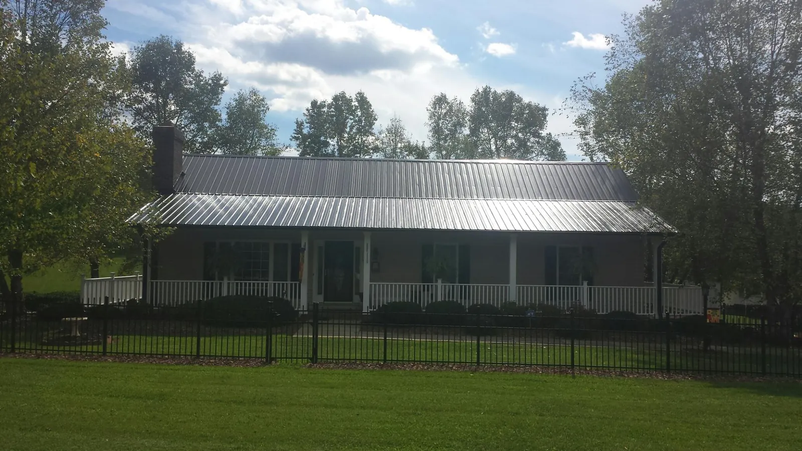 Gray metal roof on a brick ranch with a full width front porch — Gutter Guard Installation work by our crew in New Lisbon